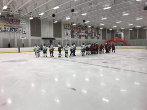 Deux équipes de hockey se remerciant pour leur participation, une fois la partie terminée, au milieu de la glace de l'aréna.
